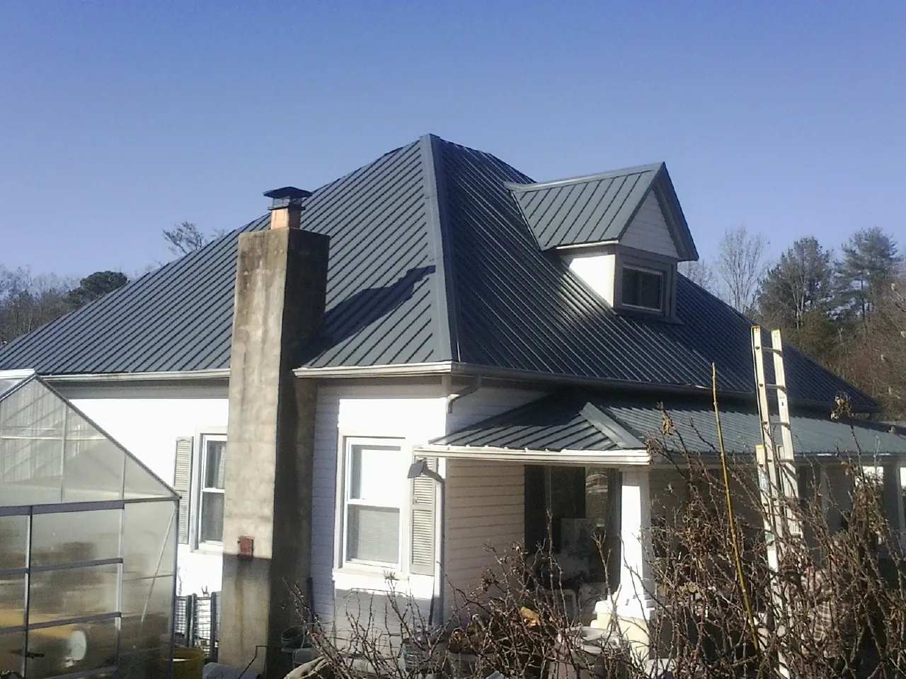 Dark blue standing seam metal roof on a white farmhouse with dormer — Slate & Tile Roof Repair by Roofing Brothers in Harvey