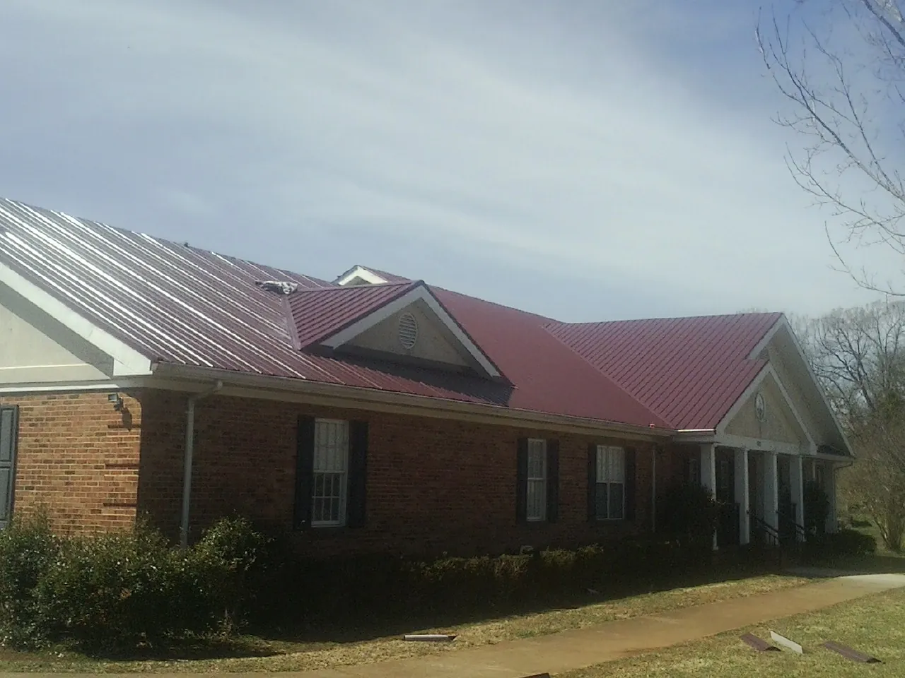 Red metal roof with gabled entries on a long brick building, from a Hail Damage Roof Repair job in Harvey
