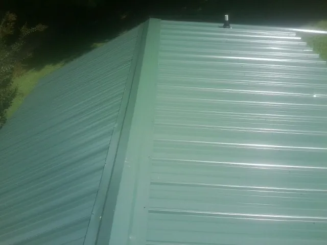 New green metal panels meeting at the ridge of a roof — Flat Roof Repair work by our crew in Harvey