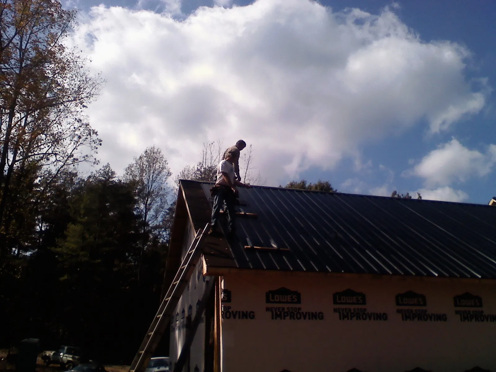 Roofer fastening dark metal panels high against a cloudy sky, from a Roof Inspection job in Harvey