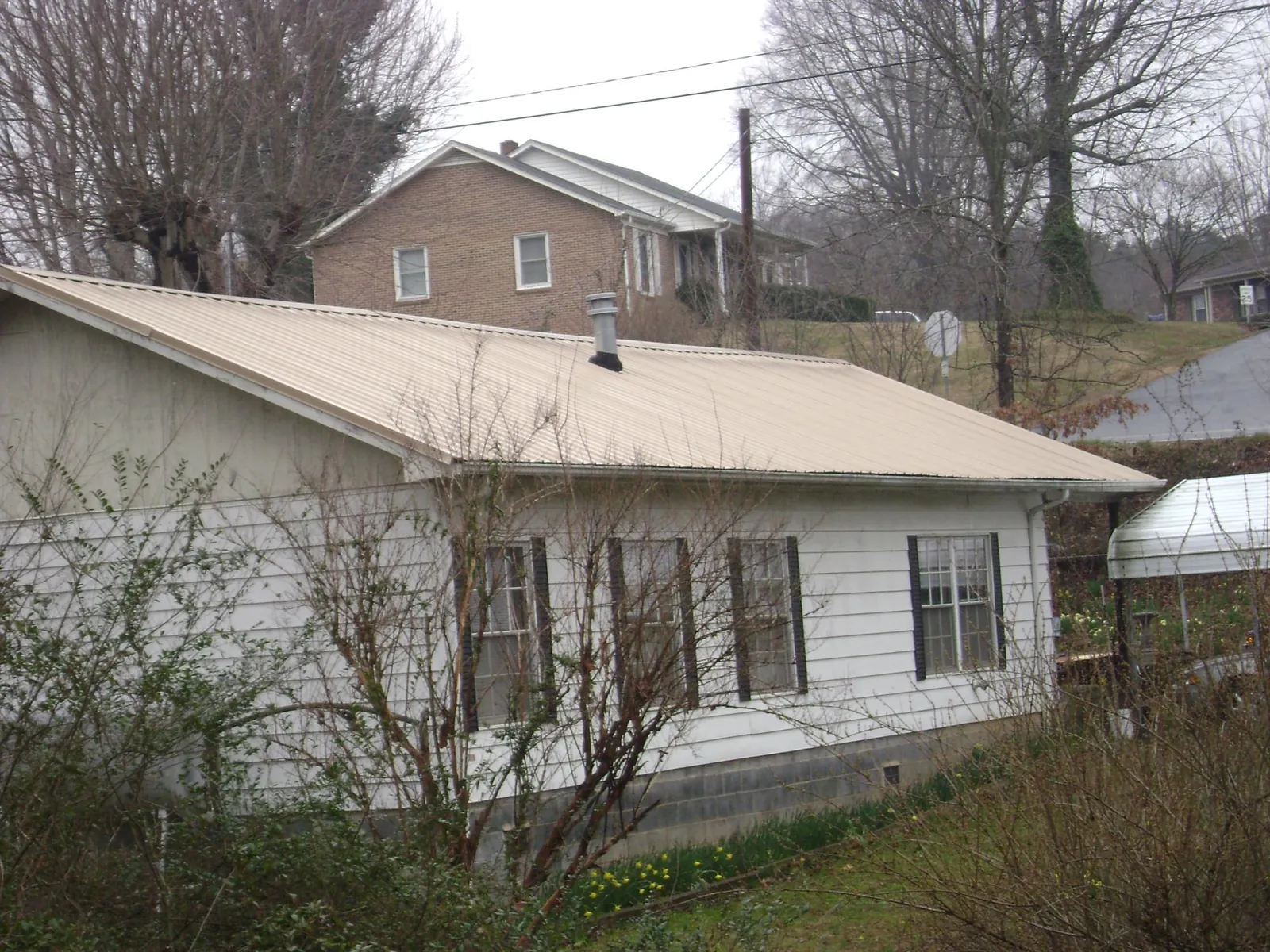 Tan metal roof on a white sided house set into a hillside — Commercial Roofing by Roofing Brothers in Harvey